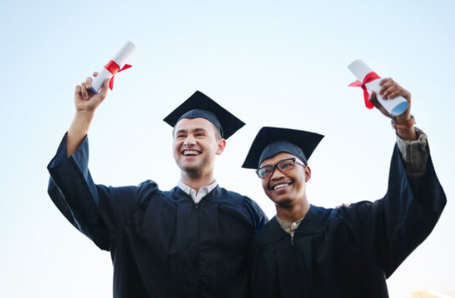 Two happy male graduates in caps and gowns holding diplomas and celebrating their achievement.